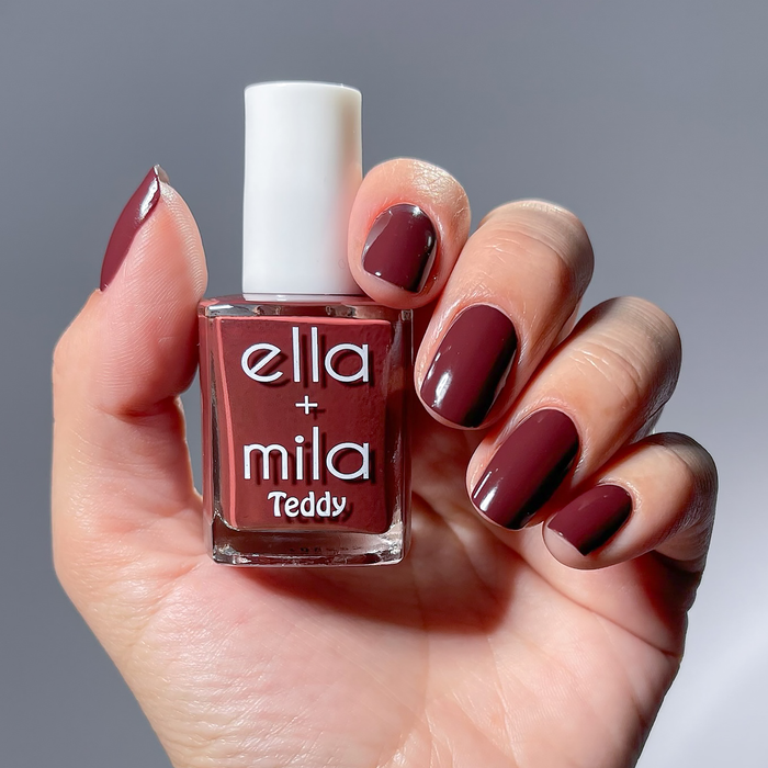 Cinnamon Swirl red brown nail polish manicure on a light skin tone, holding the bottle