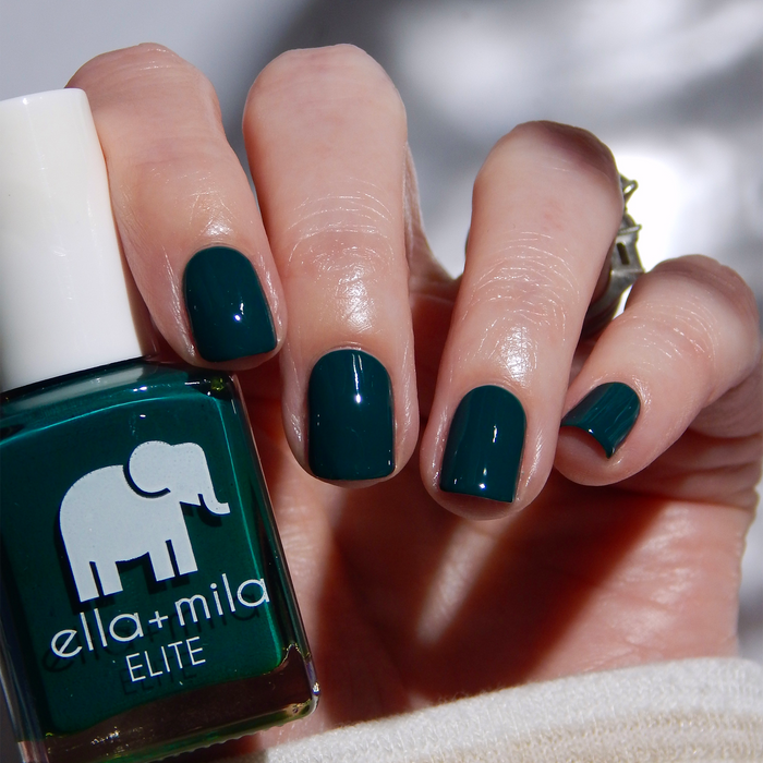 Island Hopping dark green nail polish manicure on a light skin tone, holding the bottle