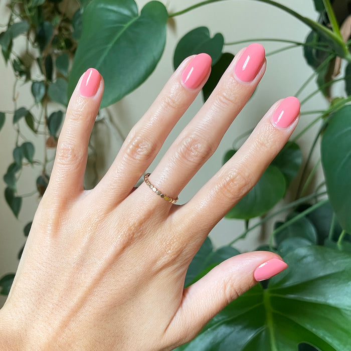 Hand with short rounded nails painted in glossy Papaya Gloss sheer coral pink polish against green leafy background