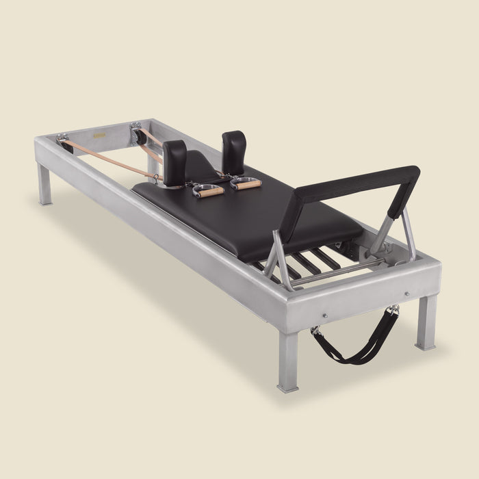 Aluminum Pilates reformer with black carriage, leather straps, and metal spring bar at the base.