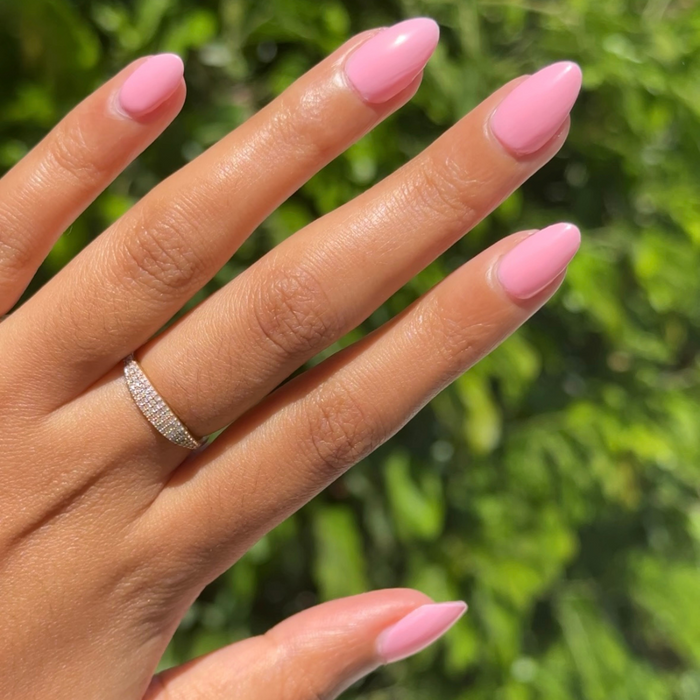 Hand with nails polished in vibrant pink Saltwater Taffy gel polish showing glossy manicure outdoors with ring on finger