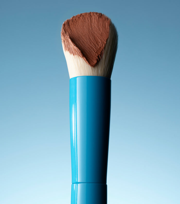 Makeup brush with brown bristle head and blue handle on a light blue background