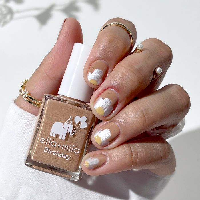 11th Hour mocha brown nail polish with white swirl accents, holding the bottle