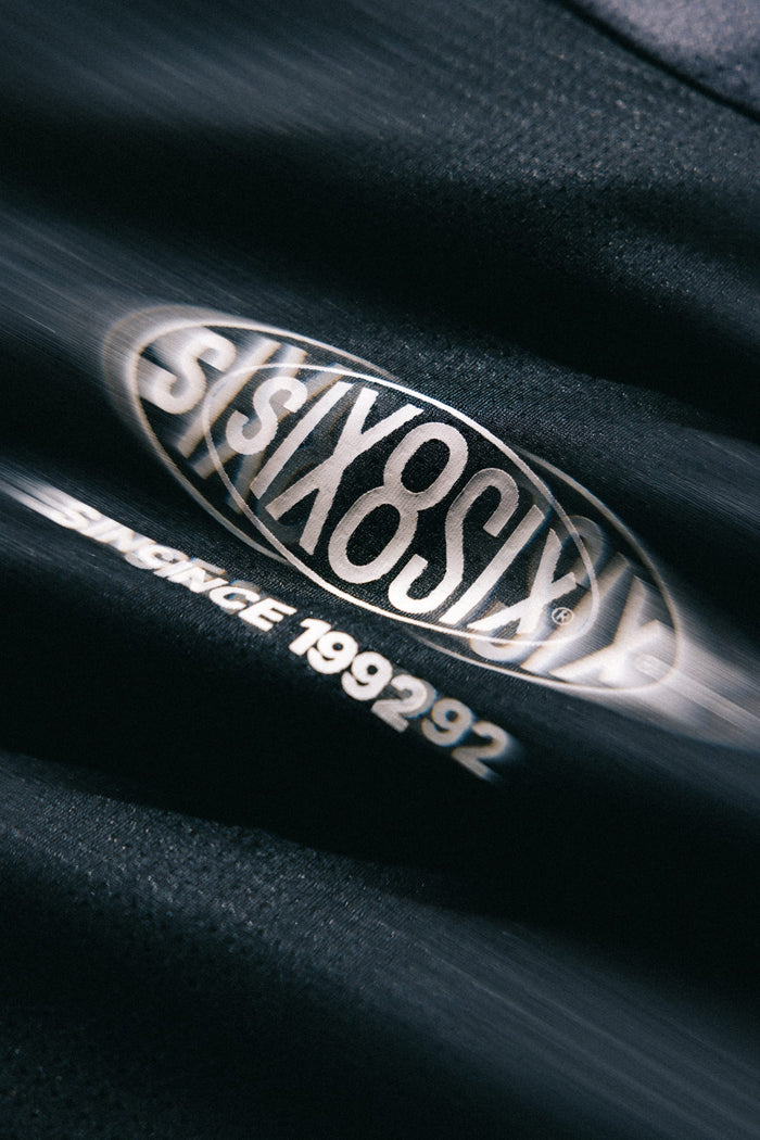 Close-up of a black 686 Men's 92 Turbo LS Tech Tee, featuring a blurred 686 logo and the text "SINCE 199292" printed below it in white letters.
