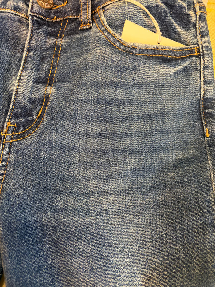 Vervet Masterfully Jean jeans hanging on a wooden background, featuring classic denim style and detailed stitching.