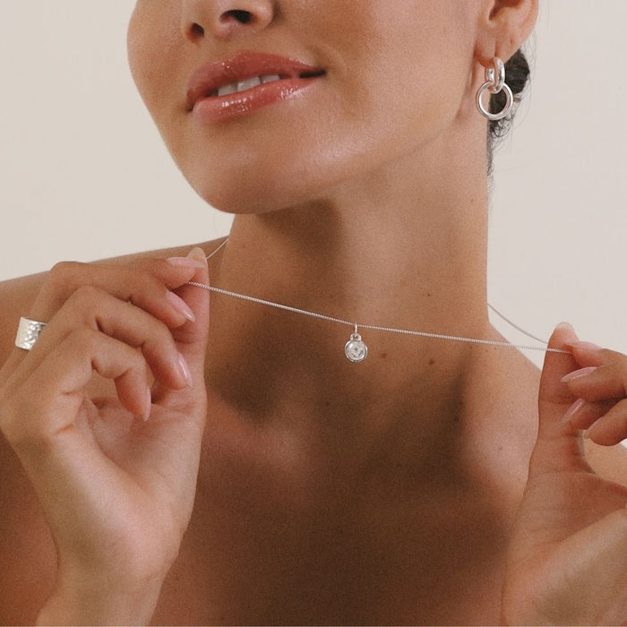 Woman adjusting a delicate silver necklace with a small pendant.