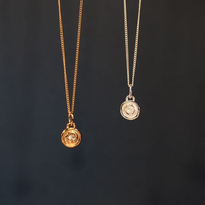 Two gold necklaces with circular pendants on a dark background
