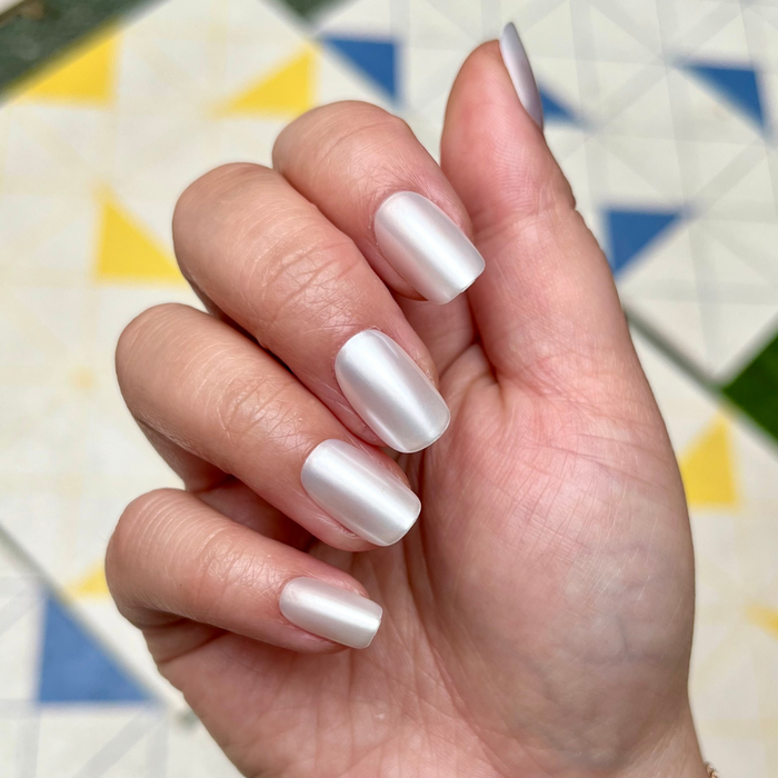 Atlas - Press-On | Short | Squoval showing hand with short squoval pearly white false nails on colorful tiled background