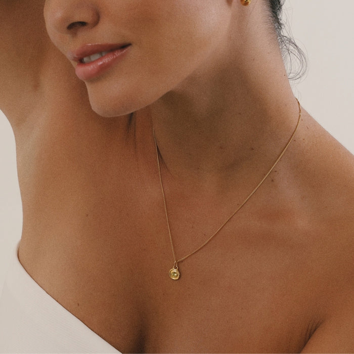Close-up of a woman wearing a gold necklace with a small round pendant.