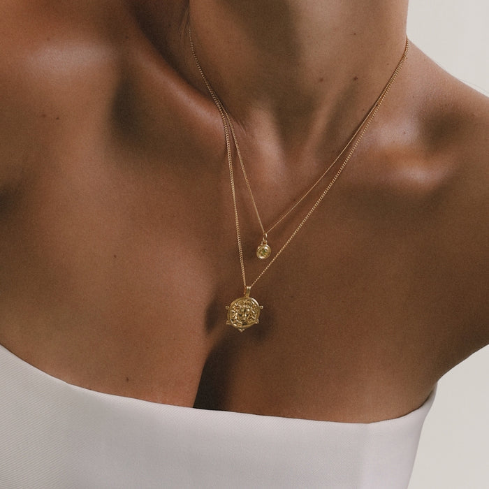 Gold necklace with a pendant on a person wearing a white top.