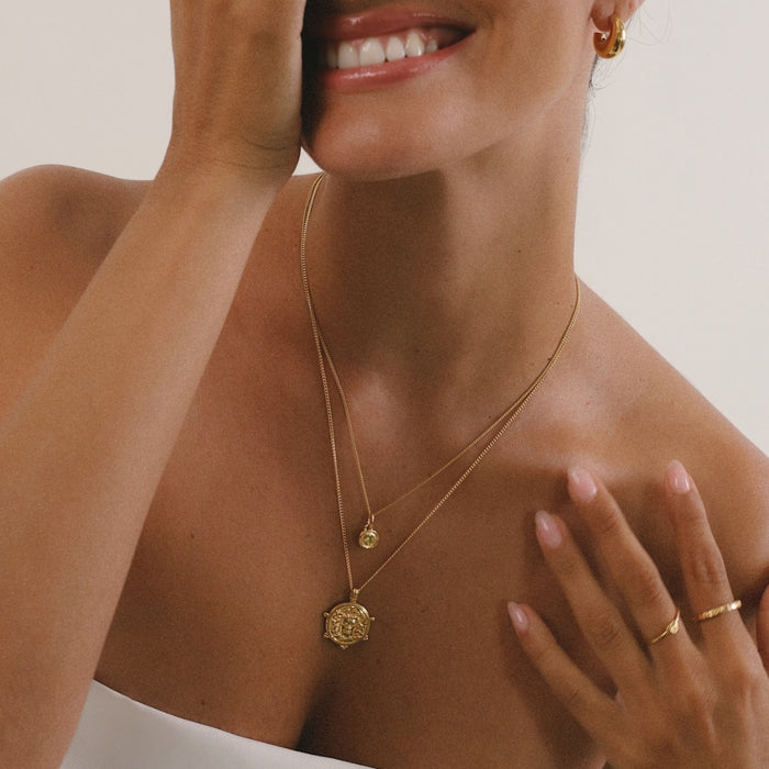 Woman wearing a gold necklace and earrings with a neutral background
