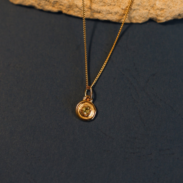 Gold necklace with a round pendant on a dark surface