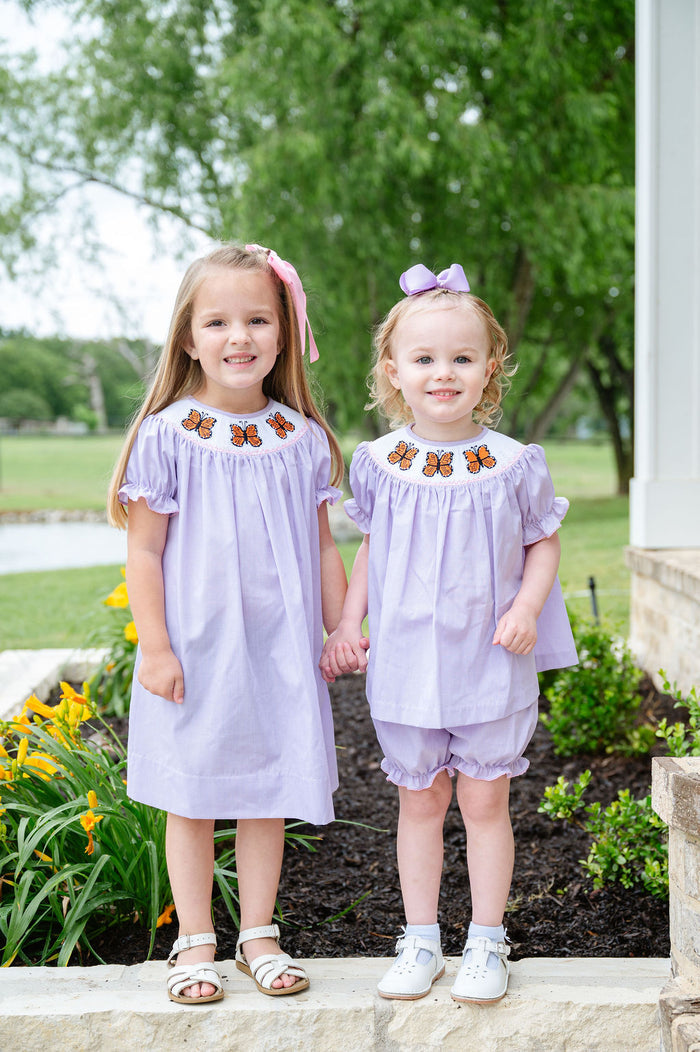 Two girls wearing matching light purple gingham smocked butterfly sets with hand-smocked orange monarch butterflies
