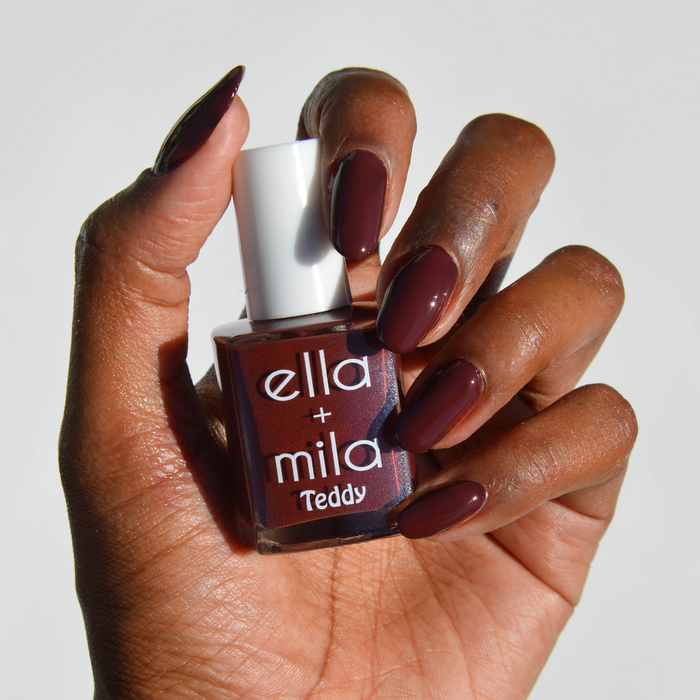 Cinnamon Swirl deep red brown nail polish on a deep skin tone, hand holding the bottle