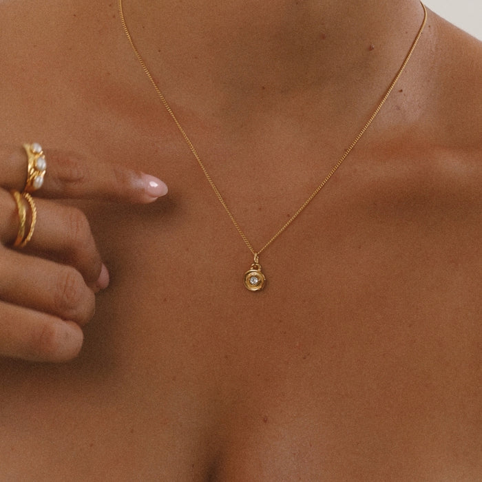 Gold necklace with a pendant on a person's neck, with a hand adjusting the necklace.