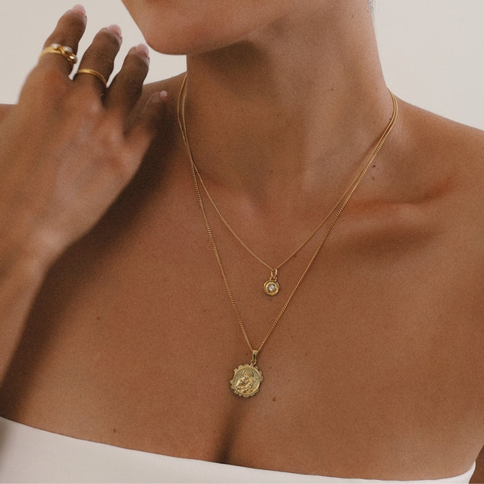 Close-up of a person wearing two gold necklaces with pendants.