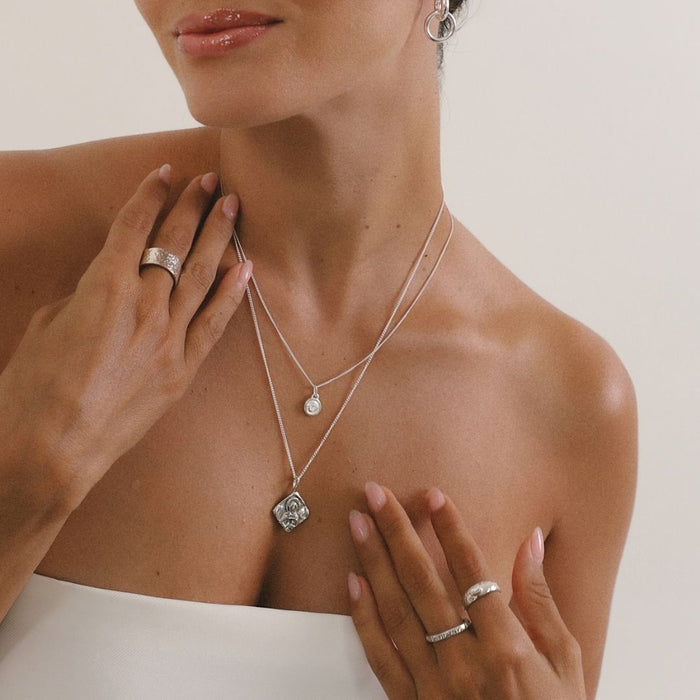 Woman wearing a silver necklace and rings on a neutral background