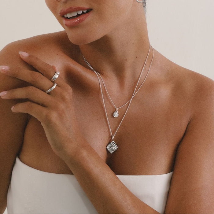 Woman wearing a silver necklace with a pendant, close-up on jewelry and skin.