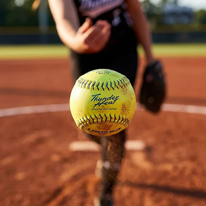 A close-up of a Dudley USSSA Thunder Heat 12" 47/375 Leather Fastpitch Softball (4U147Y) mid-air on a dirt field, with “Thunder Heat” and “Official Fast Pitch Softball” visible, and the pitcher’s blurred hand in the background.