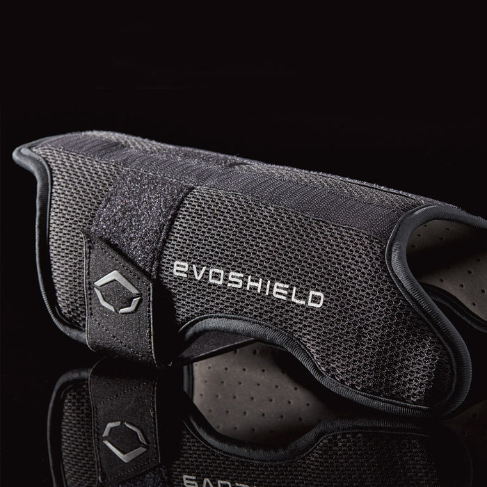 A black EvoShield Pro-SRZ Gel-to-Shell™ Catcher's Lower Leg Guard (WB570800 / WB571030) with textured mesh and Velcro strap is shown on a dark reflective surface. The EvoShield logo is visible, highlighting superior leg protection for catchers.
