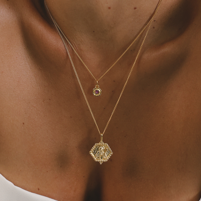Close-up of a person wearing two gold necklaces with pendants.