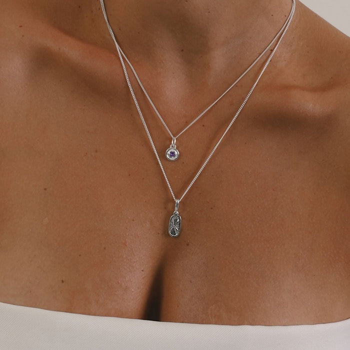 Two silver necklaces with pendants on a person's neck against a neutral background