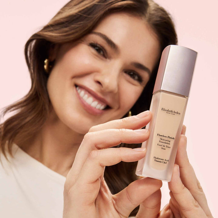 Woman holding a bottle of the Flawless Finish Skincaring Foundation against a pink background