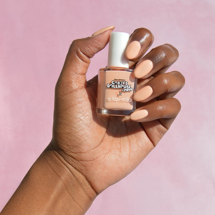 Gabby's Dollhouse Baby Box Peach nail polish on a deep skin tone, hand holding the bottle