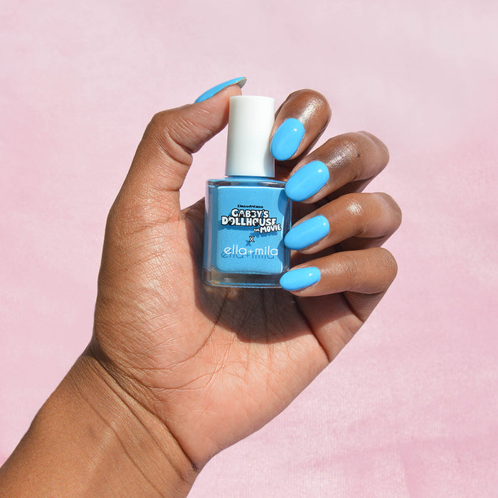 Gabby's Dollhouse CatRat Cat-i-tude sky blue nail polish on a deep skin tone, hand holding the bottle