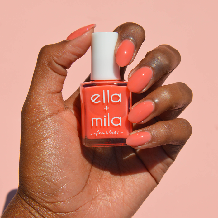 Glow Getter milky coral nail polish on a deep skin tone, hand holding the bottle