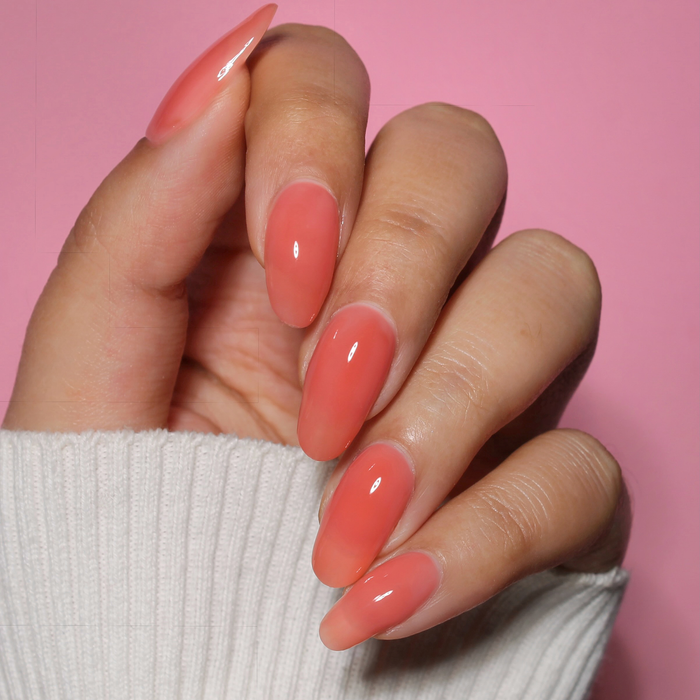 Glow Getter milky orange coral nail polish manicure on a light skin tone, pink background