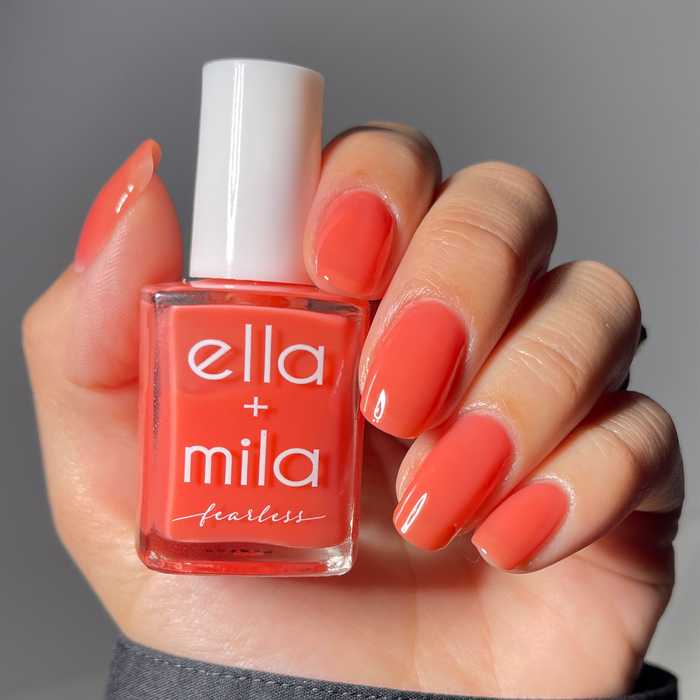 Glow Getter milky coral nail polish manicure on a light skin tone, holding the bottle