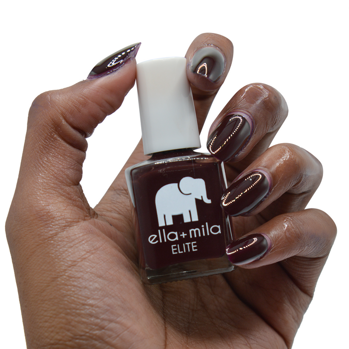 Holiday Fling dark burgundy nail polish on a deep skin tone, hand holding the bottle