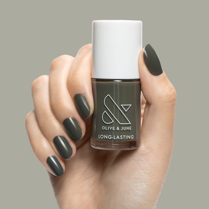 Hand holding "Is it Smoky in Here?" long-lasting gel polish with dark charcoal gray manicure on neutral background