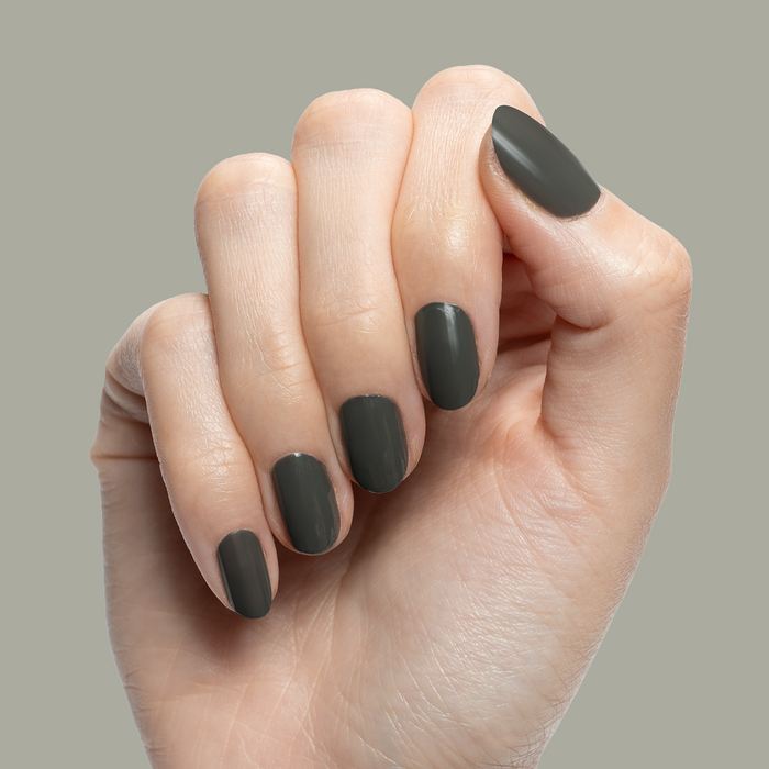 Hand showing short rounded nails painted in Is it Smoky in Here? deep charcoal gray gel polish against neutral background