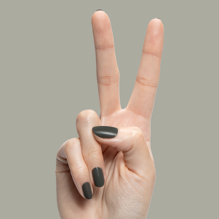 Hand with nails painted in Is it Smoky in Here? deep charcoal gray gel polish showing a peace sign on neutral background