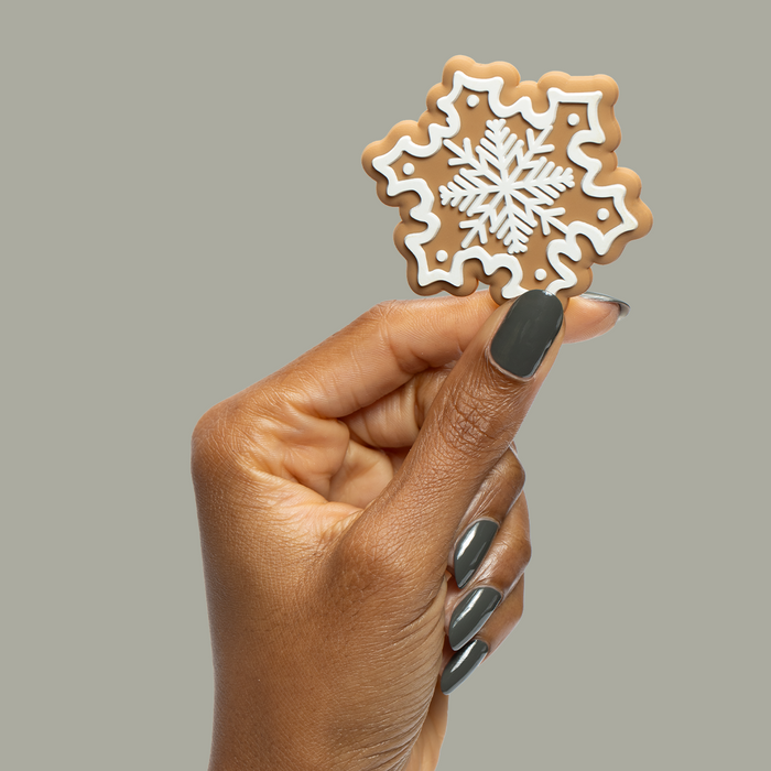 Hand with long nails painted in Is it Smoky in Here? deep charcoal gray gel polish holding snowflake cookie on gray background