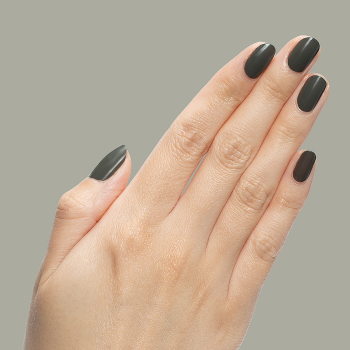 Hand with neatly shaped nails polished in "Is it Smoky in Here?" deep charcoal gray gel polish on neutral background