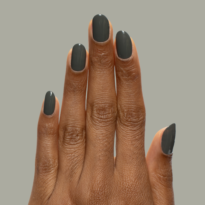 Hand with medium-length nails painted in Is it Smoky in Here? deep charcoal gray gel polish on neutral background