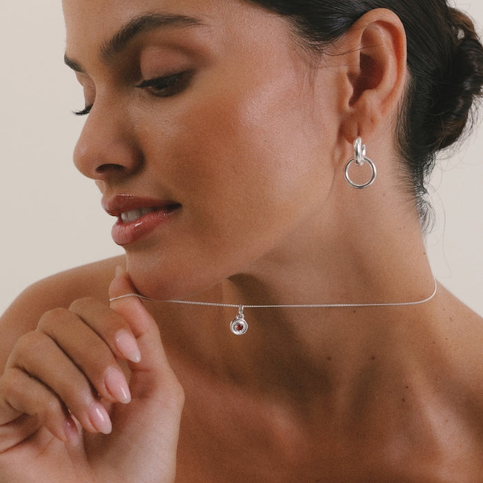 Woman wearing a silver necklace and earrings against a neutral background