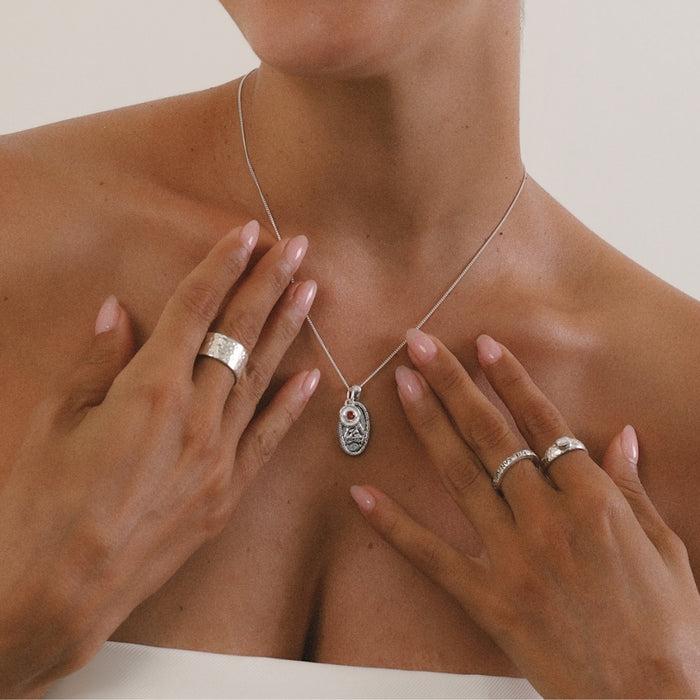 Person wearing a silver necklace with a pendant, hands adjusting it, on a neutral background