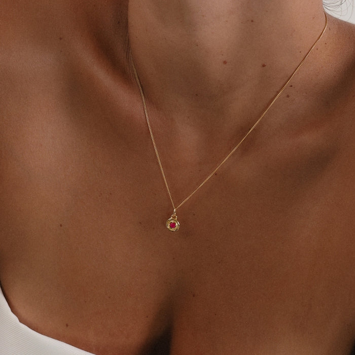 Gold necklace with a red gemstone pendant on a person's neck