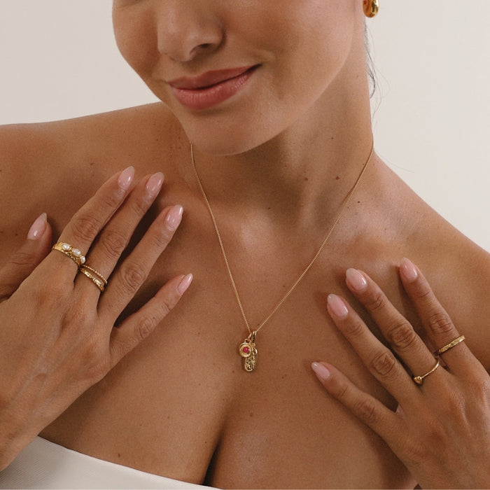 Woman wearing a gold necklace with a pendant, surrounded by hands with gold rings.