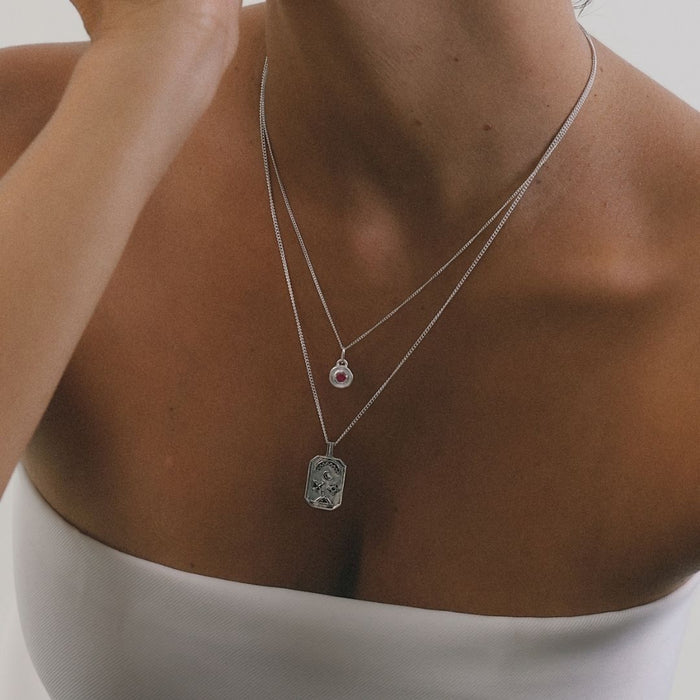Close-up of a person wearing two silver necklaces with pendants on a neutral background