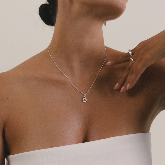 Woman wearing a silver necklace with a pink gemstone, with a hand adjusting it.