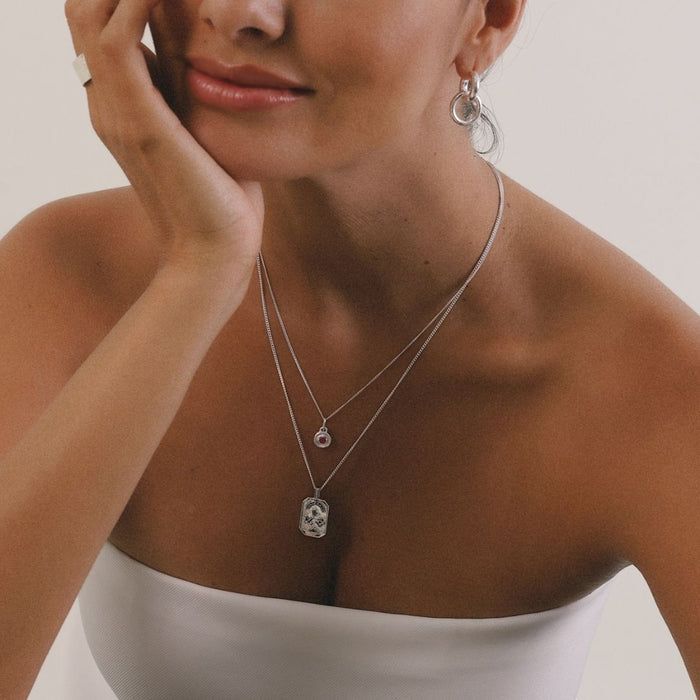 Woman wearing a silver necklace with a pendant, close-up of her neck and chest.