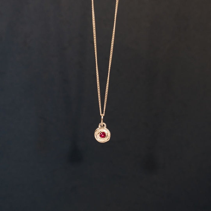 Gold necklace with a red gemstone pendant on a dark background
