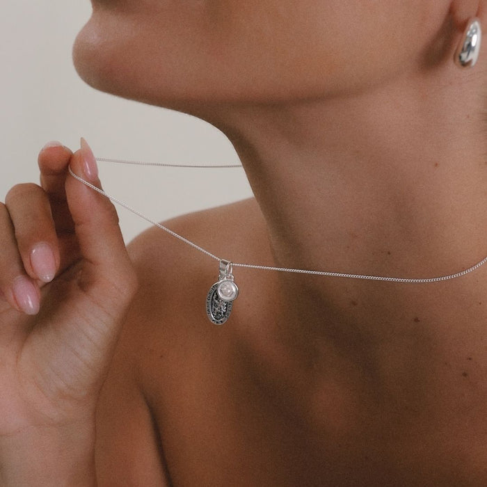 Close-up of a silver necklace with a pendant being held by a hand.
