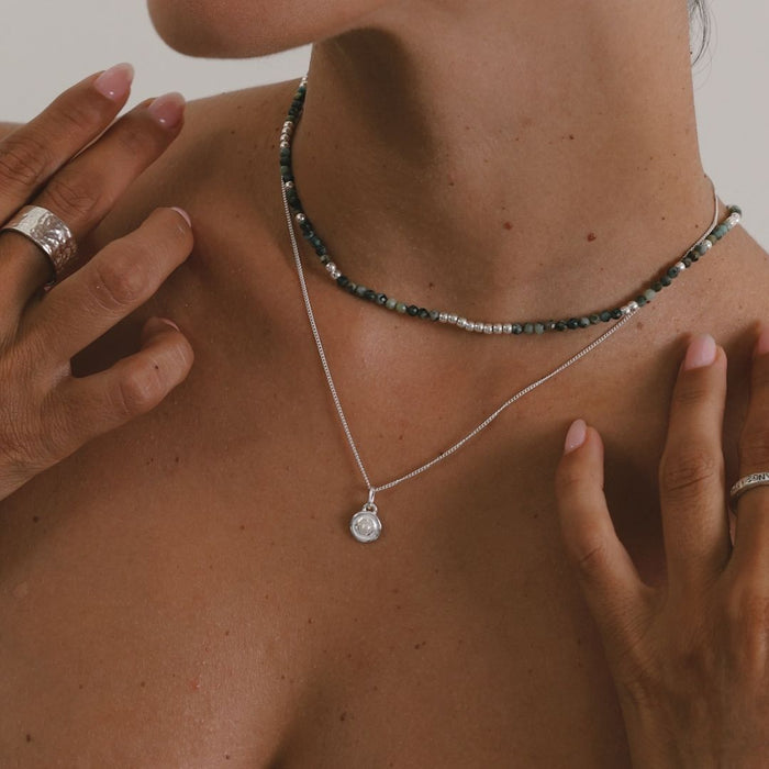 Close-up of a person wearing two necklaces with a neutral background