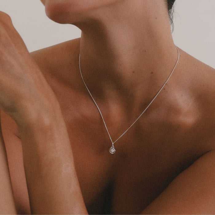Close-up of a necklace with a pendant on a person's neck against a neutral background